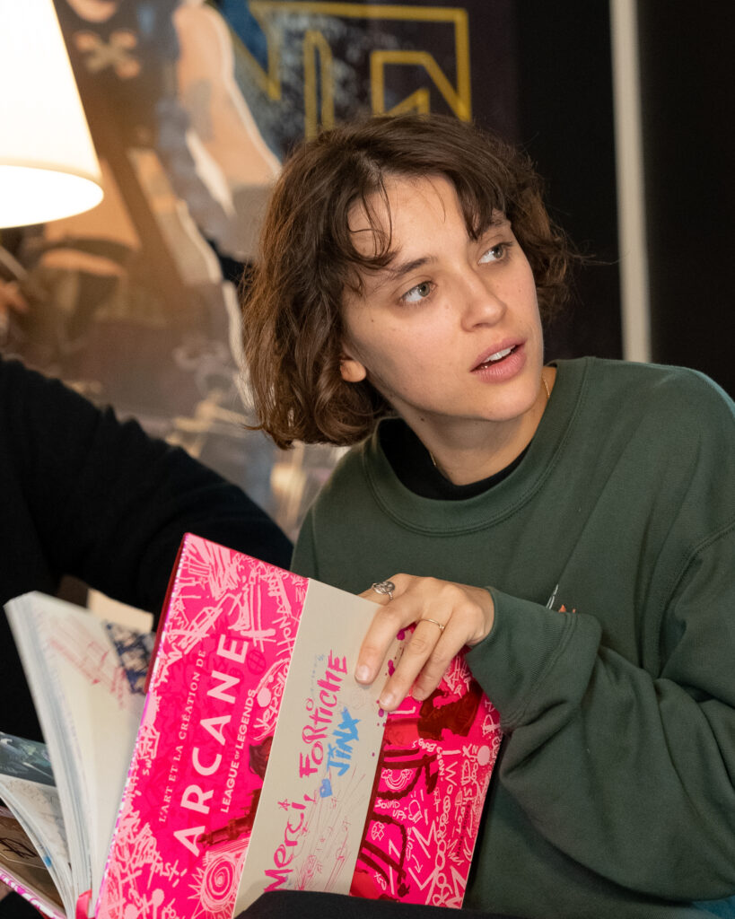 Singer-songwriter Pomme holding a signed "The Art and Making of Arcane" book at Fortiche, for celebrating Ma Meilleure Ennemie.